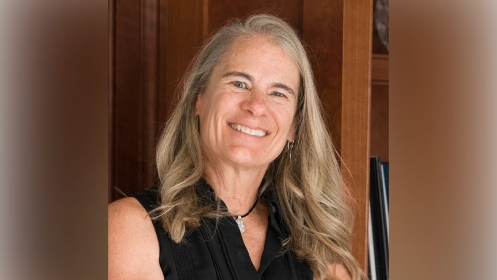 Portrait of Kendall Webb, founder of Charity Bridge Fund, smiling in front of wooden bookshelves