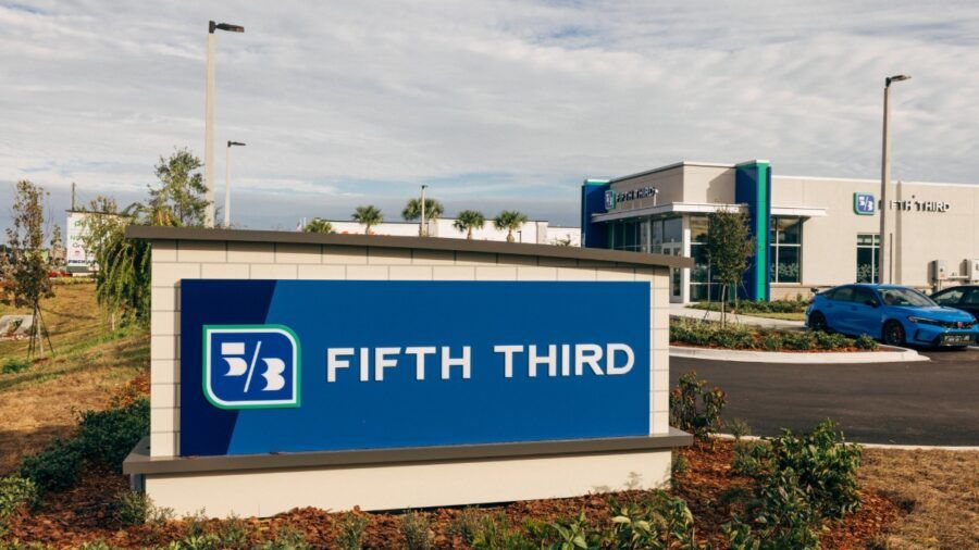 Modern exterior of a Fifth Third Bank branch with glass walls, green accents and a bright blue sky.