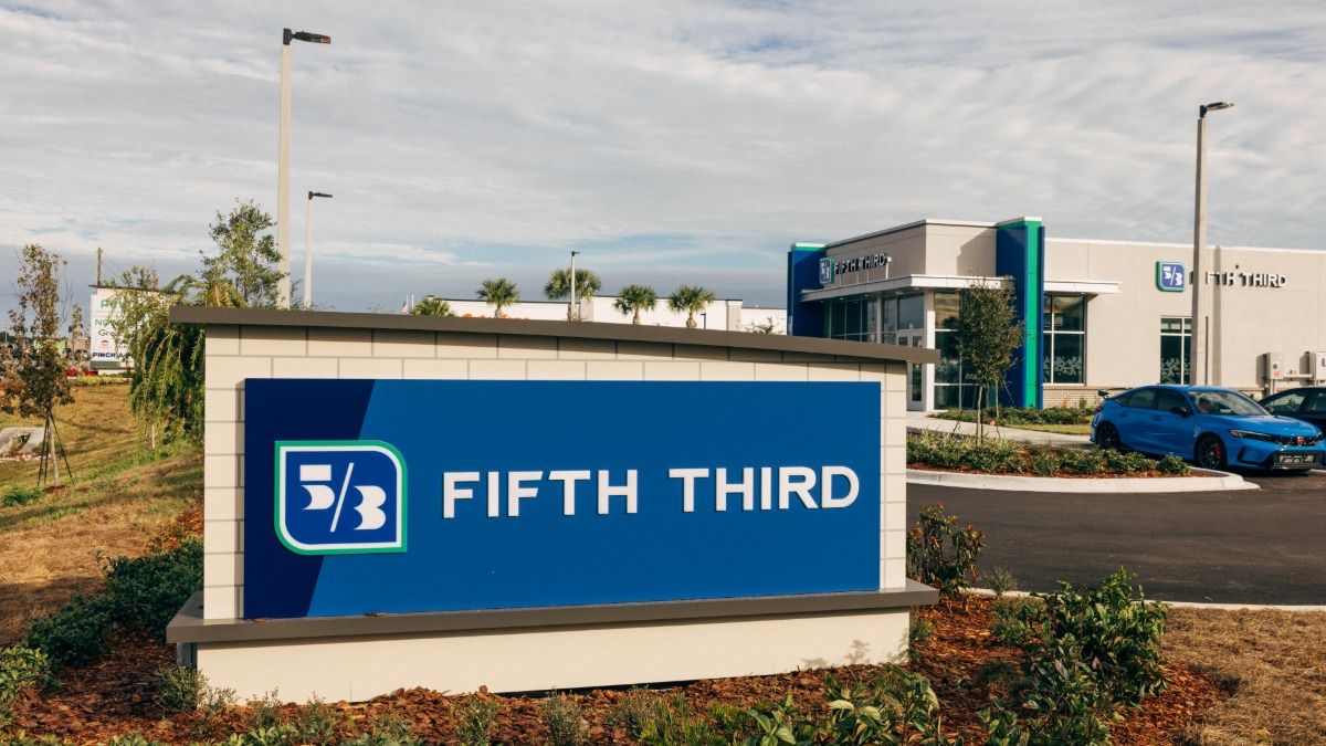 Modern exterior of a Fifth Third Bank branch with glass walls, green accents and a bright blue sky.