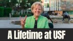 Dr. Rhea Law sits on the University of South Florida campus, smiling and flashing the Bull Horns hand sign near the USF Bull statues.