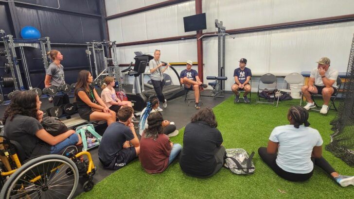 Students and clinicians sit in a circle during a behavioral health session inside a gym-style facility