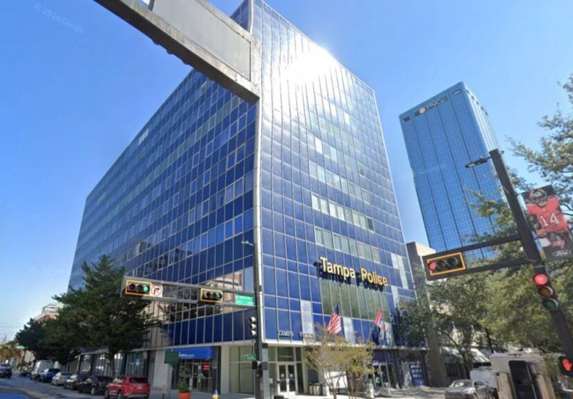 Tampa Police officers standing in a line in front of the Tampa Police Department headquarters, a tall blue-glass building in downtown Tampa.