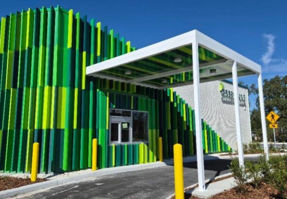 Greenlane drive-thru restaurant exterior with green panel facade and roadside sign under a bright blue sky.