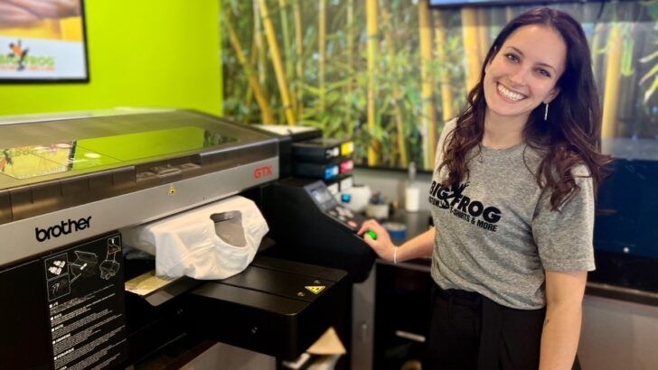 A Big Frog franchisee stands beside a direct-to-garment printer