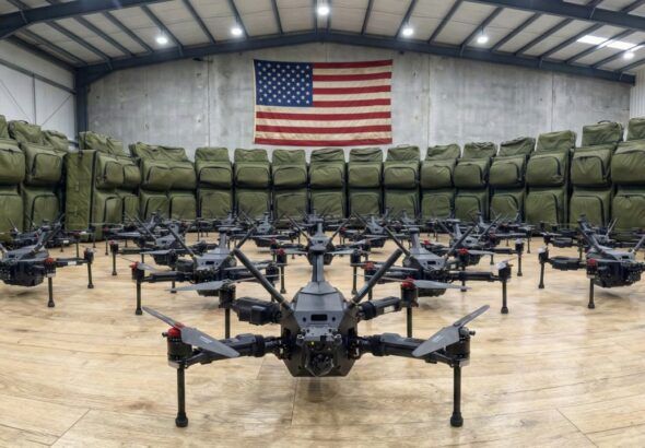 Rows of XTEND drone systems arranged inside a warehouse with a large American flag displayed on the back wall.