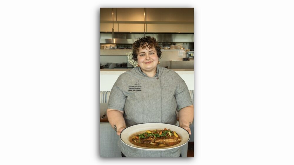 Chef de cuisine Shelby Farrell holding a plated dish inside the Oystercatchers kitchen