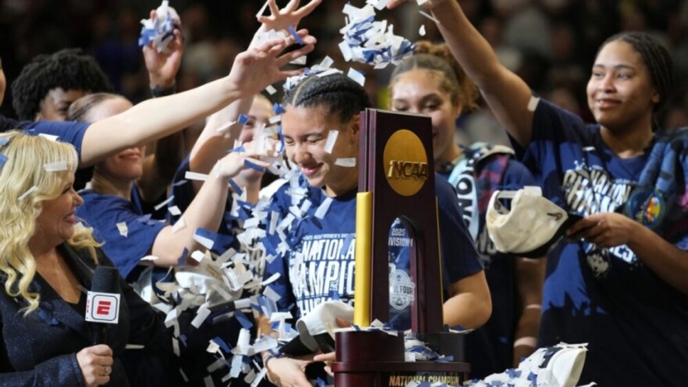 UConn players celebrate winning the NCAA Women’s Final Four championship as confetti falls around the national championship trophy.