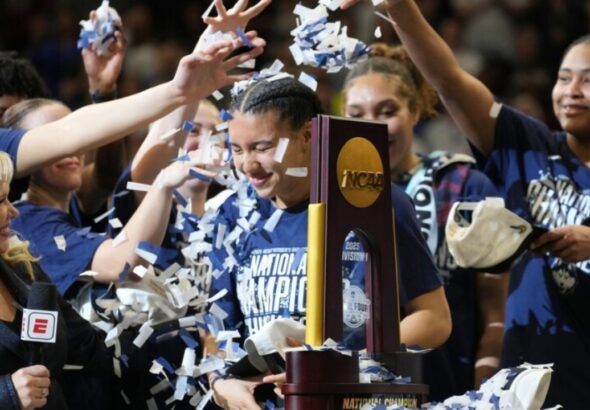 UConn players celebrate winning the NCAA Women’s Final Four championship as confetti falls around the national championship trophy.