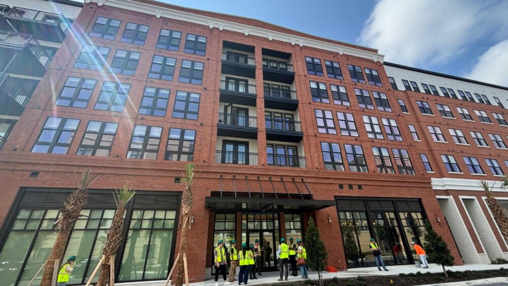 The Stevedore apartment building at Gasworx in Ybor City, a mid-rise brick residential development with ground-floor retail and workers gathered outside during a site tour.
