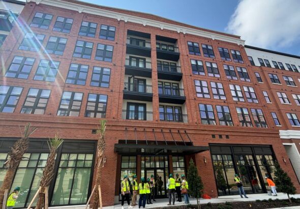 The Stevedore apartment building at Gasworx in Ybor City, a mid-rise brick residential development with ground-floor retail and workers gathered outside during a site tour.