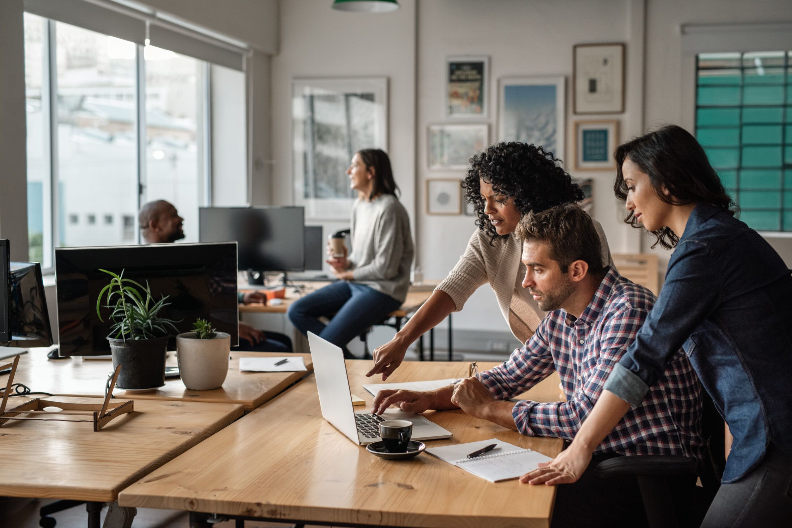 Office workers collaborate around a laptop in a modern workspace