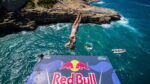 Cliff diver midair above rocky coastline in Polignano a Mare during Red Bull Cliff Diving World Series.
