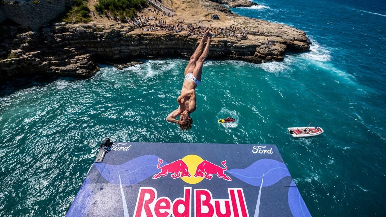 Cliff diver midair above rocky coastline in Polignano a Mare during Red Bull Cliff Diving World Series.