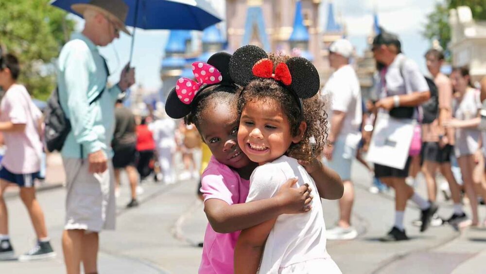 Two children wearing Minnie Mouse ears hug in front of Cinderella Castle at Walt Disney World