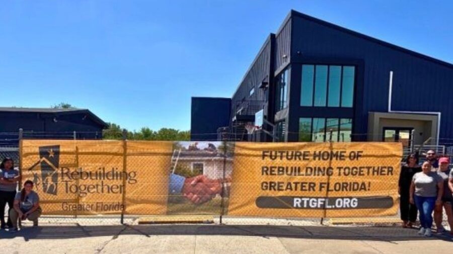 Rebuilding Together Greater Florida team stands outside its new Ybor City headquarters with banner announcing future home