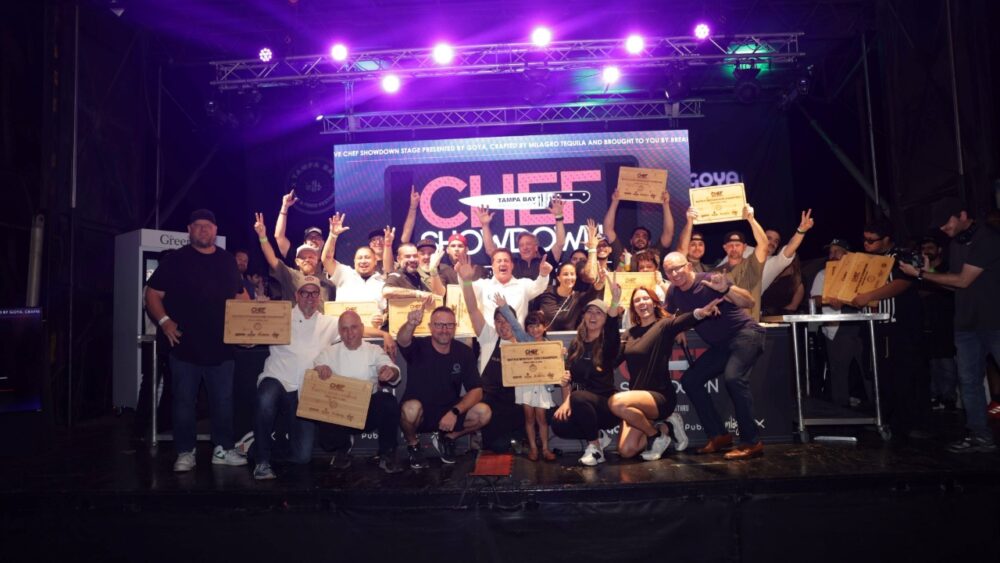 Chefs and participants celebrate on stage during the Tampa Bay Wine & Food Festival Chef Showdown, holding awards.