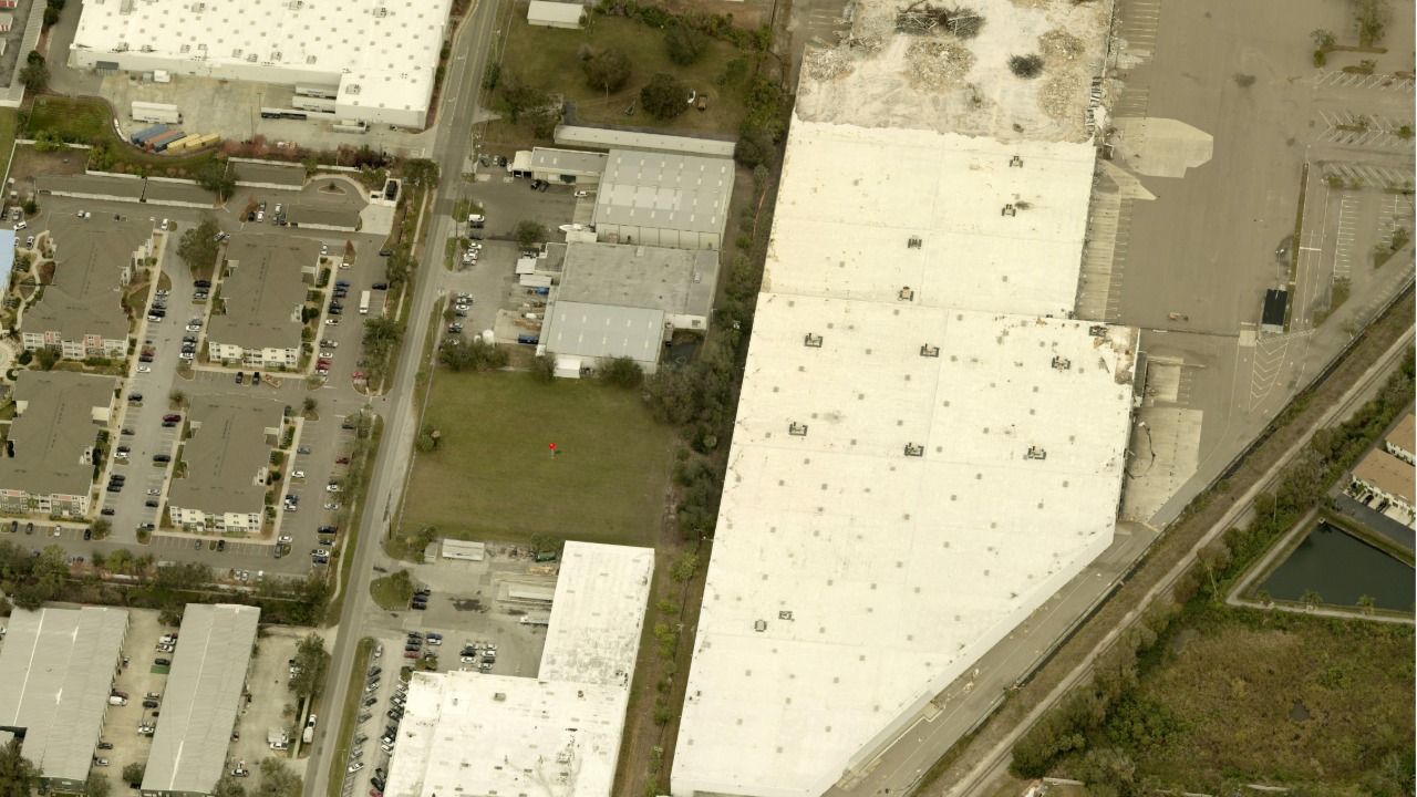 Aerial view of a vacant industrial lot at the corner of S Lois Avenue and W Pearl Avenue in Tampa, surrounded by warehouses and apartment complexes.