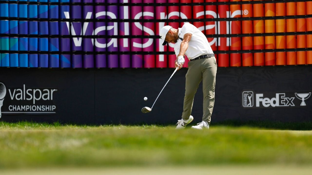 Golfer tees off during the Valspar Championship in front of a large Valspar-branded display.