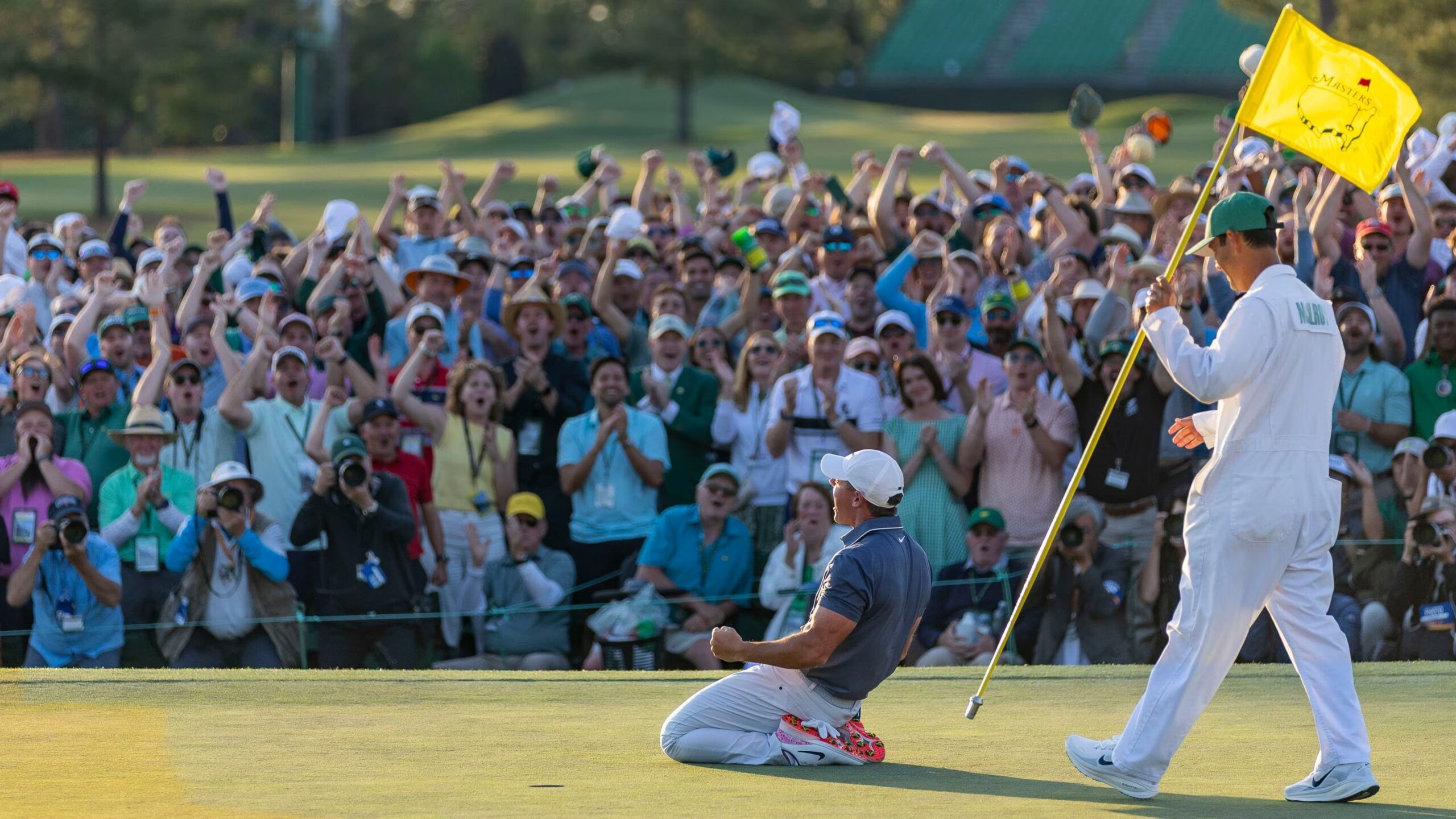Rory McIlroy celebrates after winning the Masters Tournament at Augusta National Golf Club, completing the career Grand Slam as patrons cheer behind the 18th green.