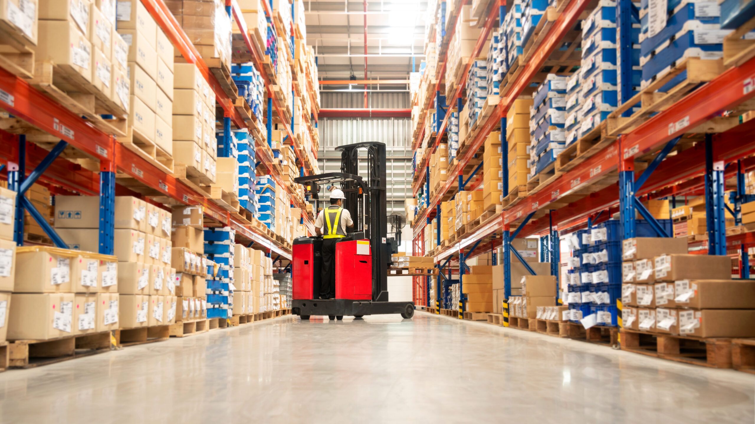 Warehouse worker operating a forklift between rows of pallet racks filled with boxes