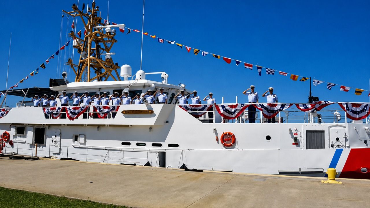 Coast Guard crew members stand aboard a cutter decorated with signal flags and patriotic bunting.