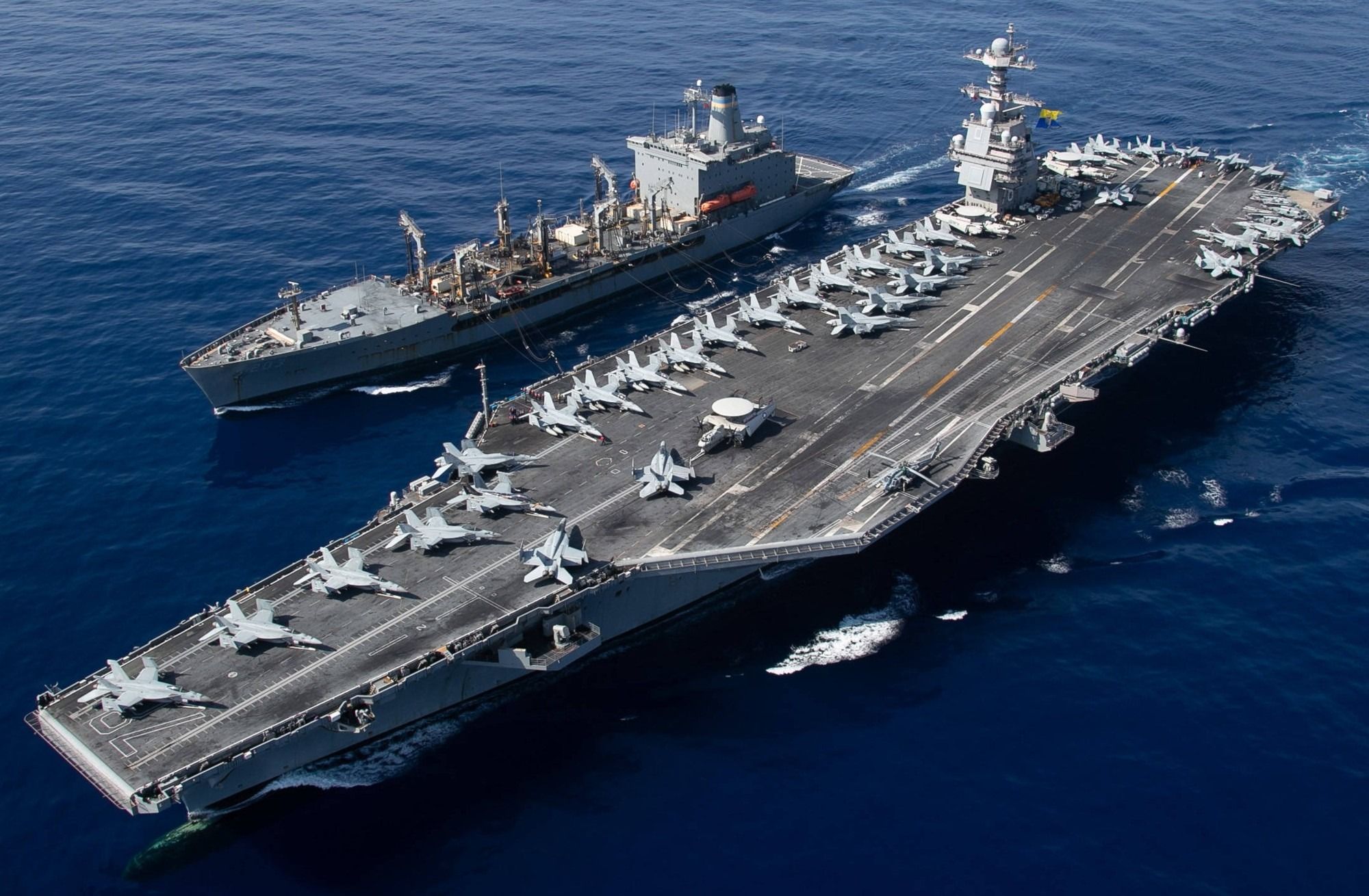U.S. Navy aircraft carrier underway at sea alongside a replenishment ship, with aircraft positioned across the flight deck.