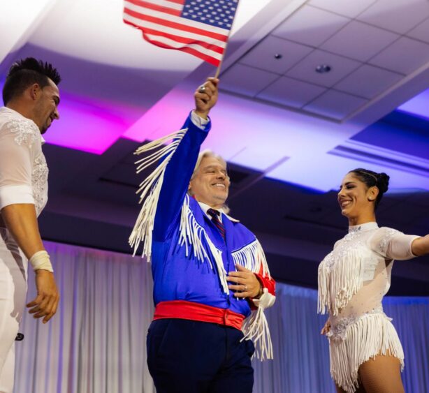 Santiago Corrada waves an American flag onstage while standing between two performers at a Visit Tampa Bay event.