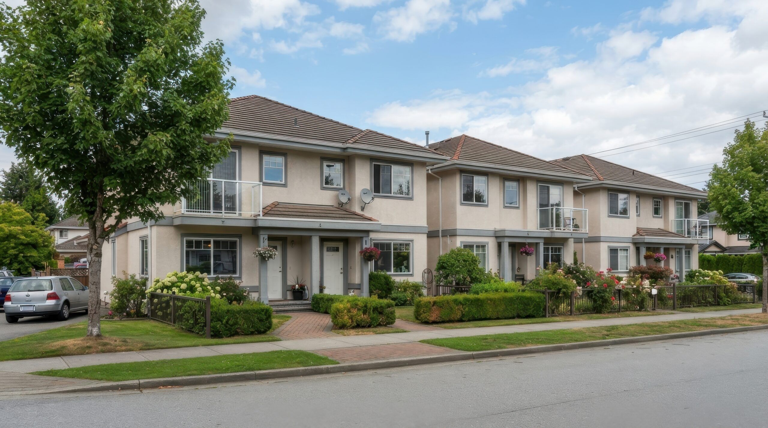 Two-story townhomes with balconies, landscaped front yards and a sidewalk along a residential street.