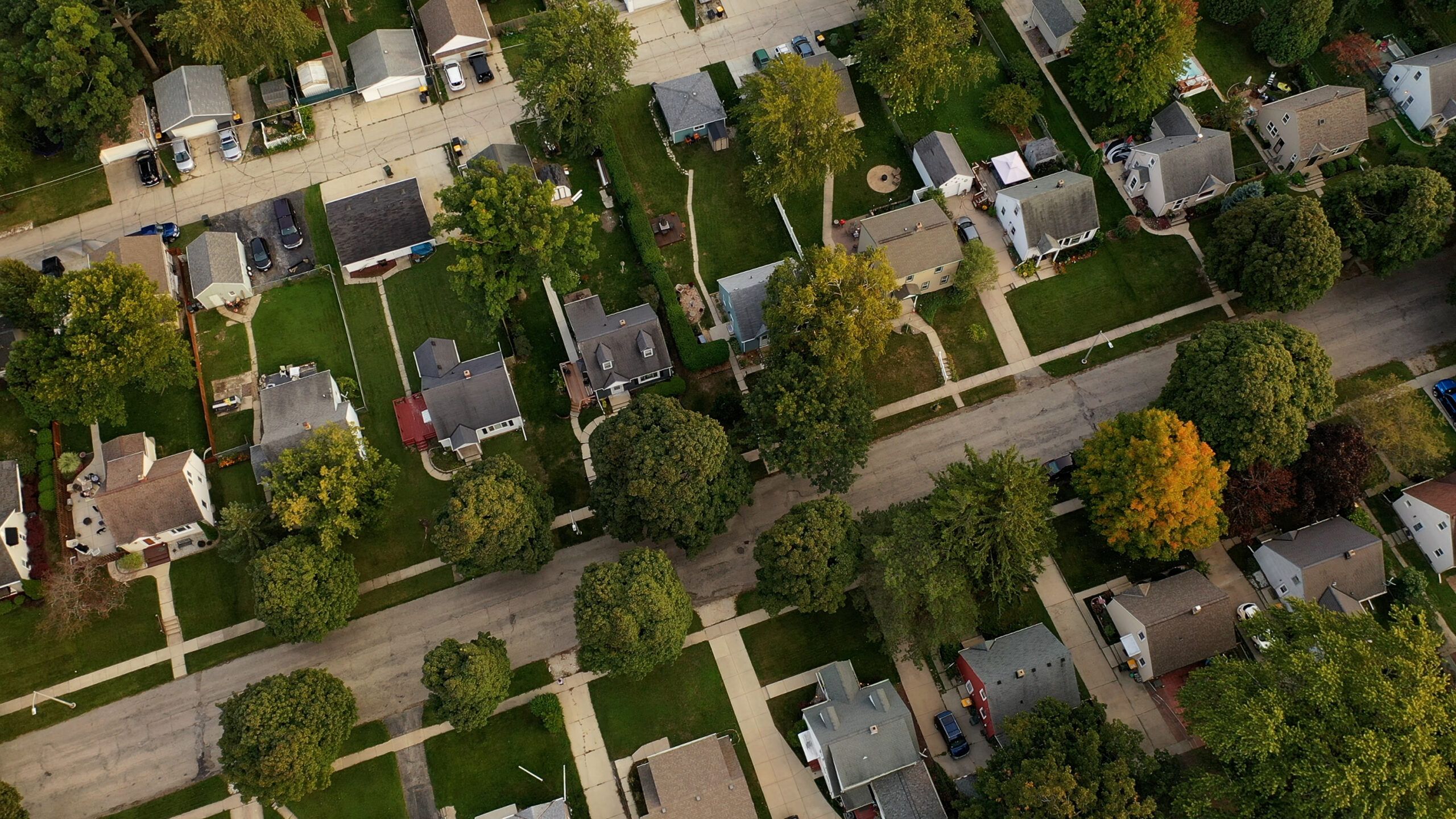 Aerial view of a residential neighborhood with single-family homes, tree-lined streets, driveways and lawns.