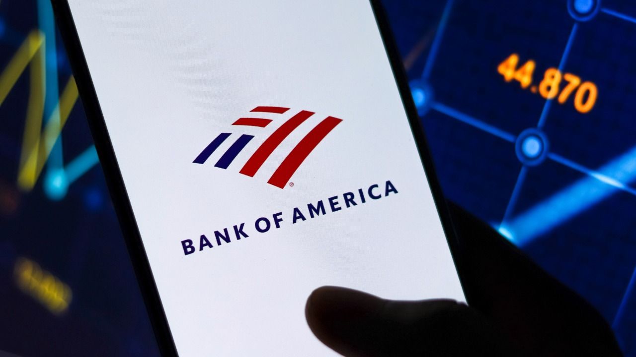 Bank of America logo displayed on a smartphone against a blue financial market background.